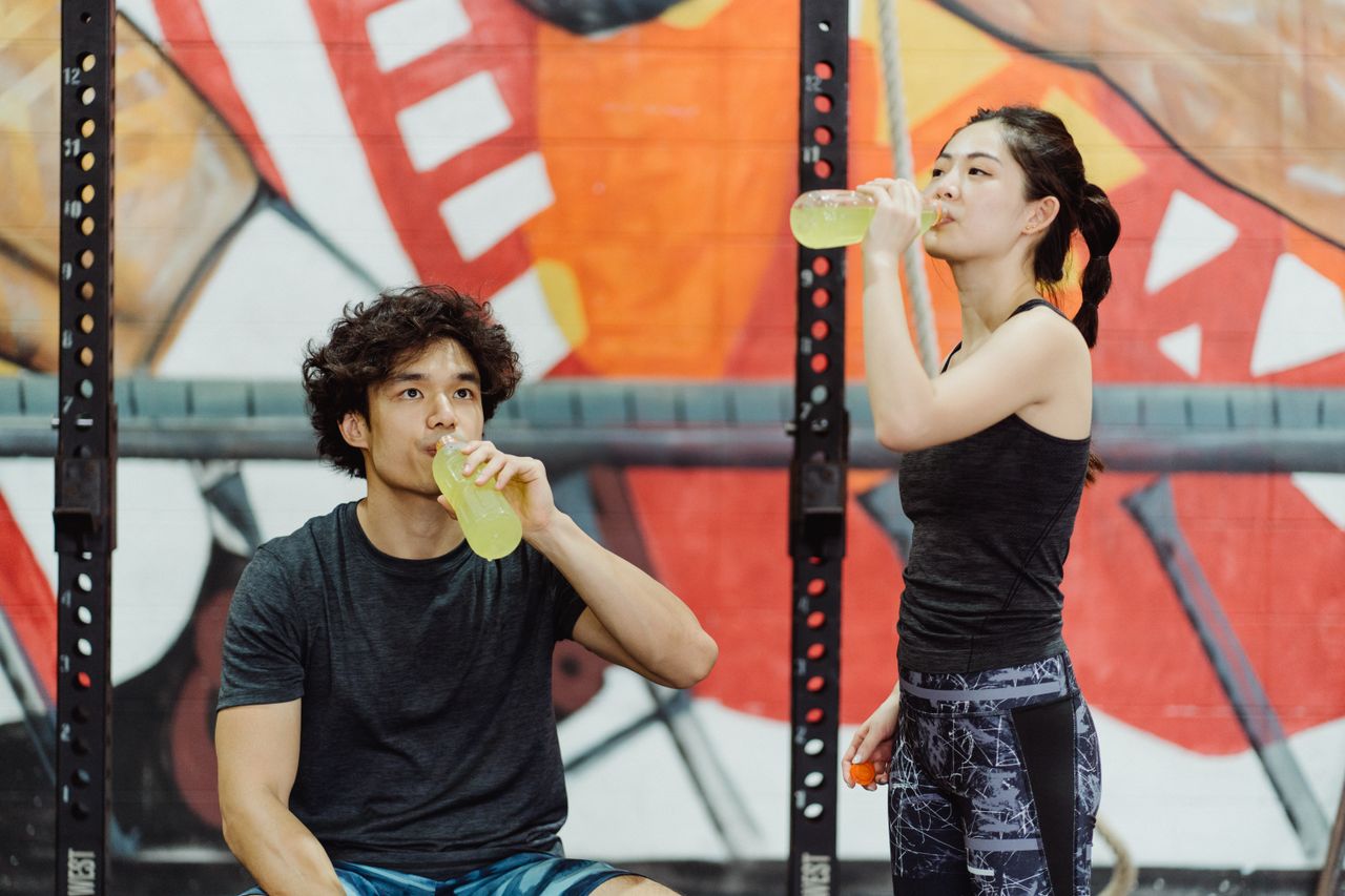 Asian couple in activewear drinking yellow beverages at an indoor gym.